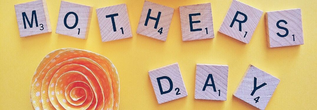 Close Up of Scrabble Tiles Spelling Mother's Day on Yellow Background