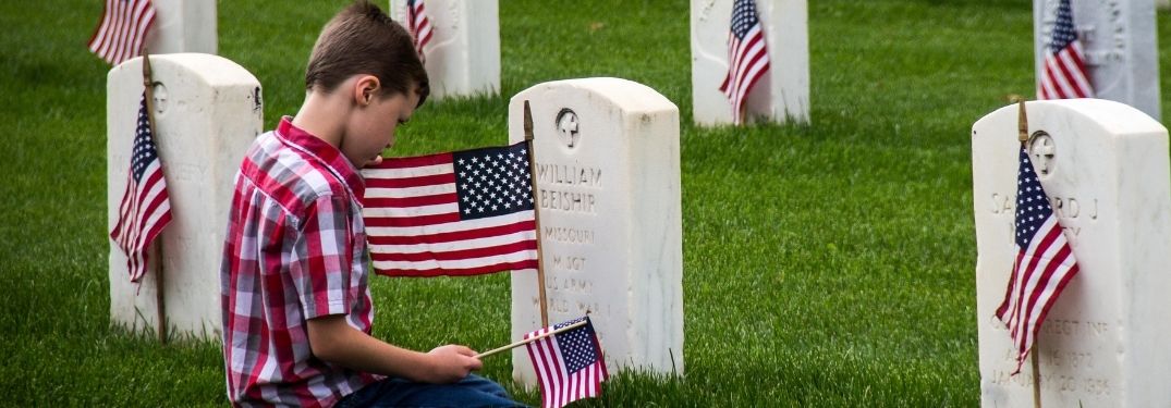 Boy Kneeling by Military Headstone with American Flag