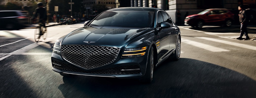 A close up view of the front of a 2022 Genesis G80 parked in a city street, with pedestrians in the background