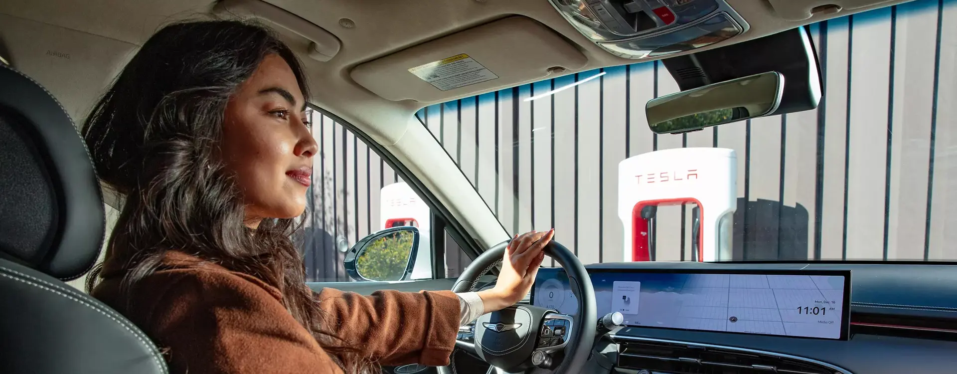 Interior passenger view of driver holding the steering wheel while parked at a charging station