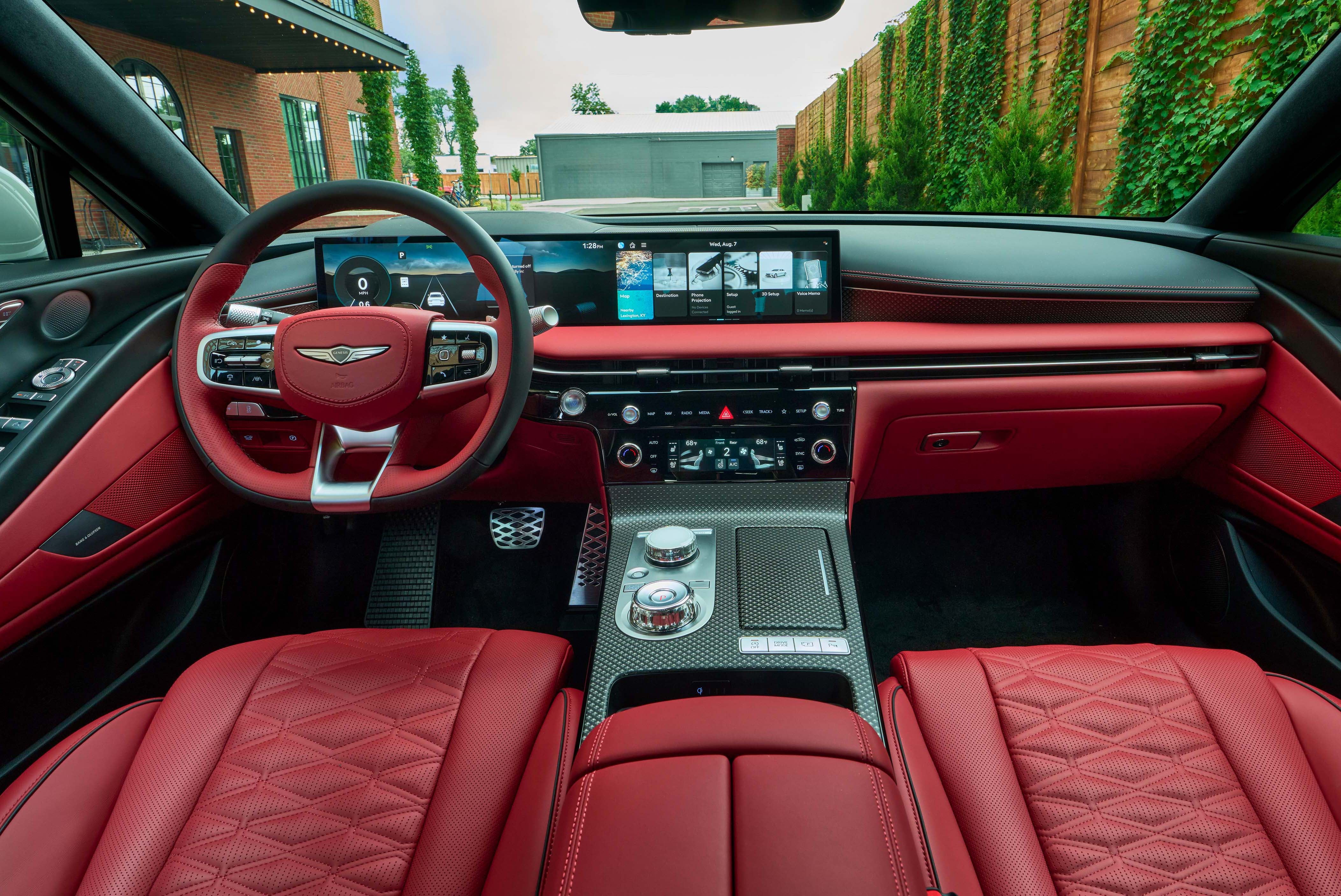The interior of a car, showing the dashboard, steering wheel, and seats. The interior is red and black, with a large digital display screen across the dashboard.