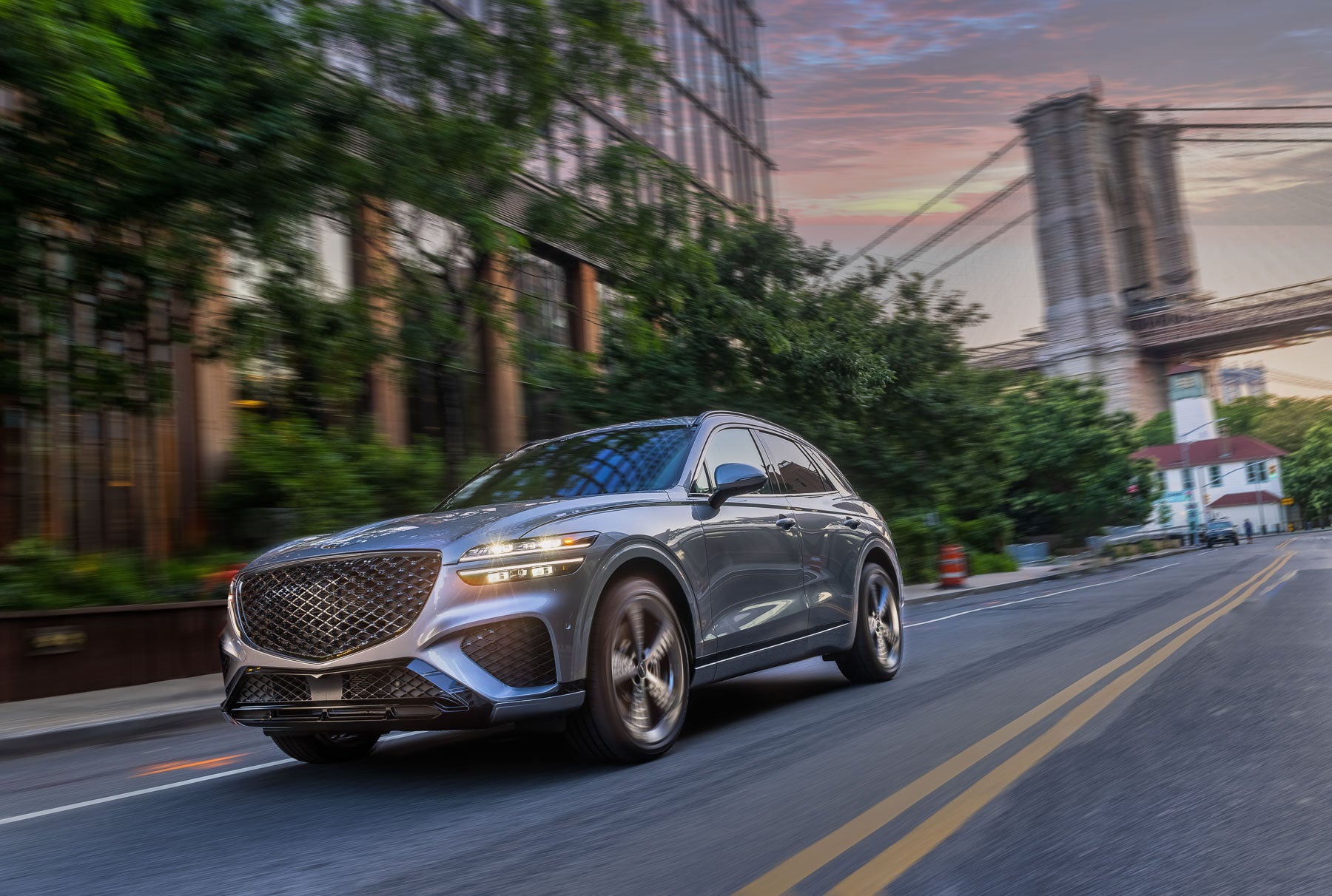 Genesis GV70 driving through a city at dusk.