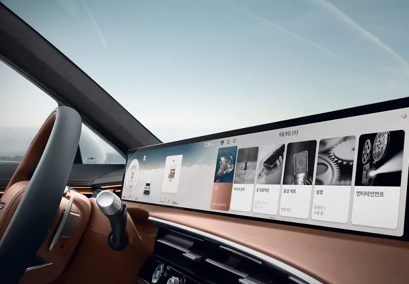 Alt text: "The interior of a Genesis vehicle featuring a wide, curved infotainment display with a sleek user interface, set against a brown leather dashboard and a modern steering wheel."