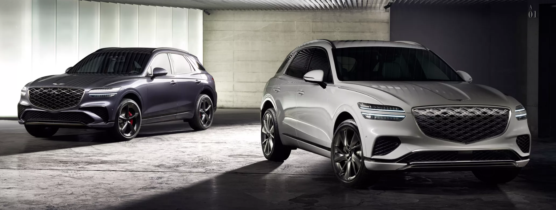"Two Genesis GV70 SUVs in a modern showroom—one silver in the foreground and one dark metallic in the background—showcasing their sleek design, signature grille, and LED headlights."