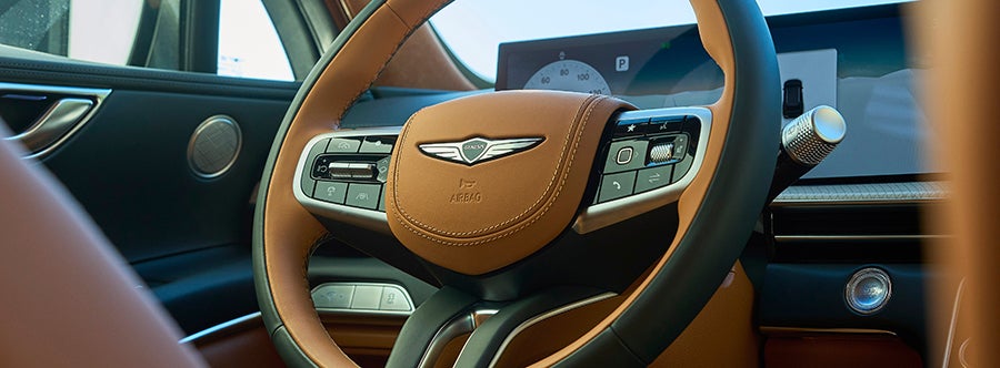 A brown leather steering wheel with the Genesis logo.