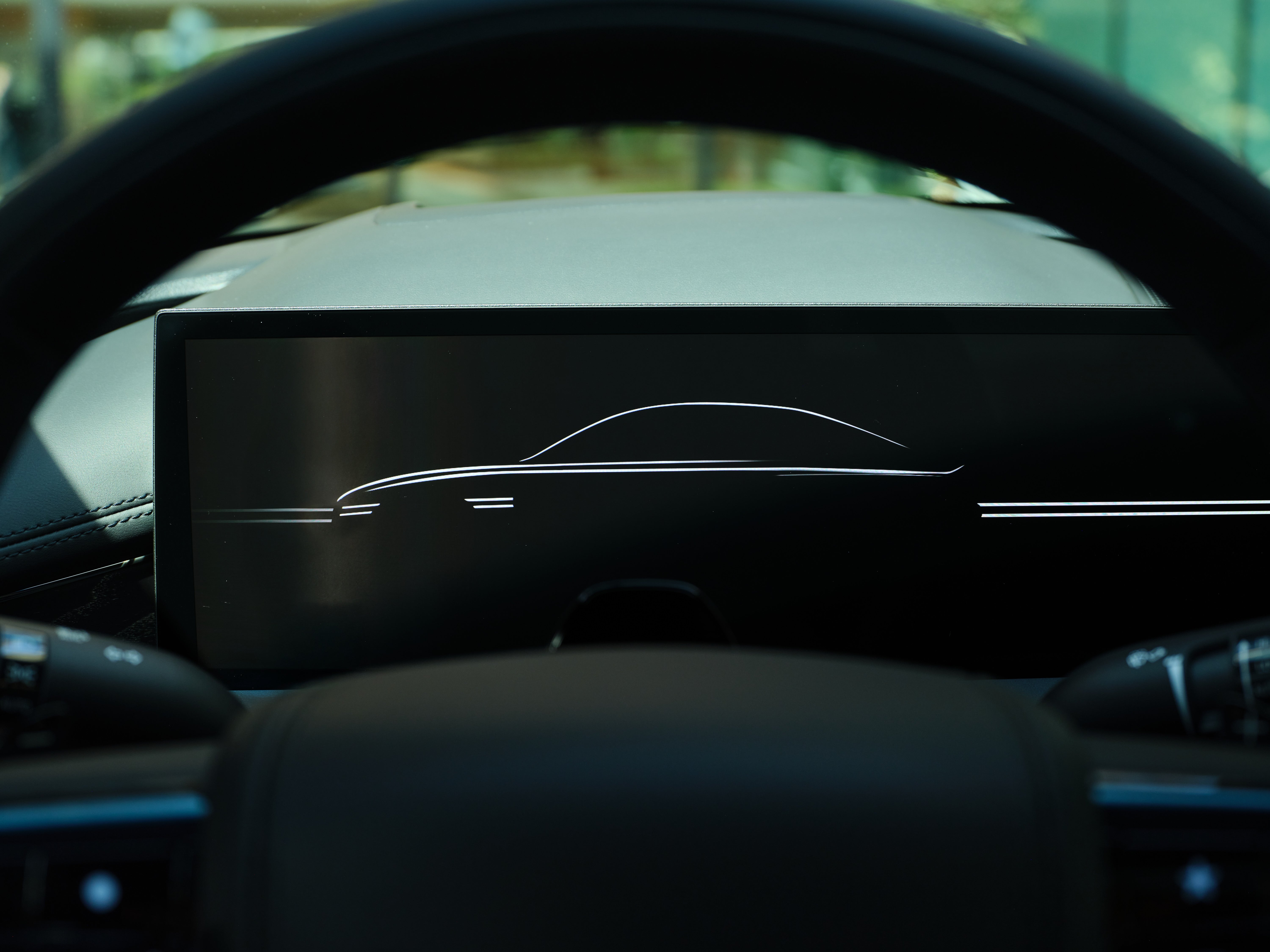 The large touchscreen of the 2026 G80 in Scottsdale is viewed through the steering wheel, displaying a side view of the Genesis sedan.