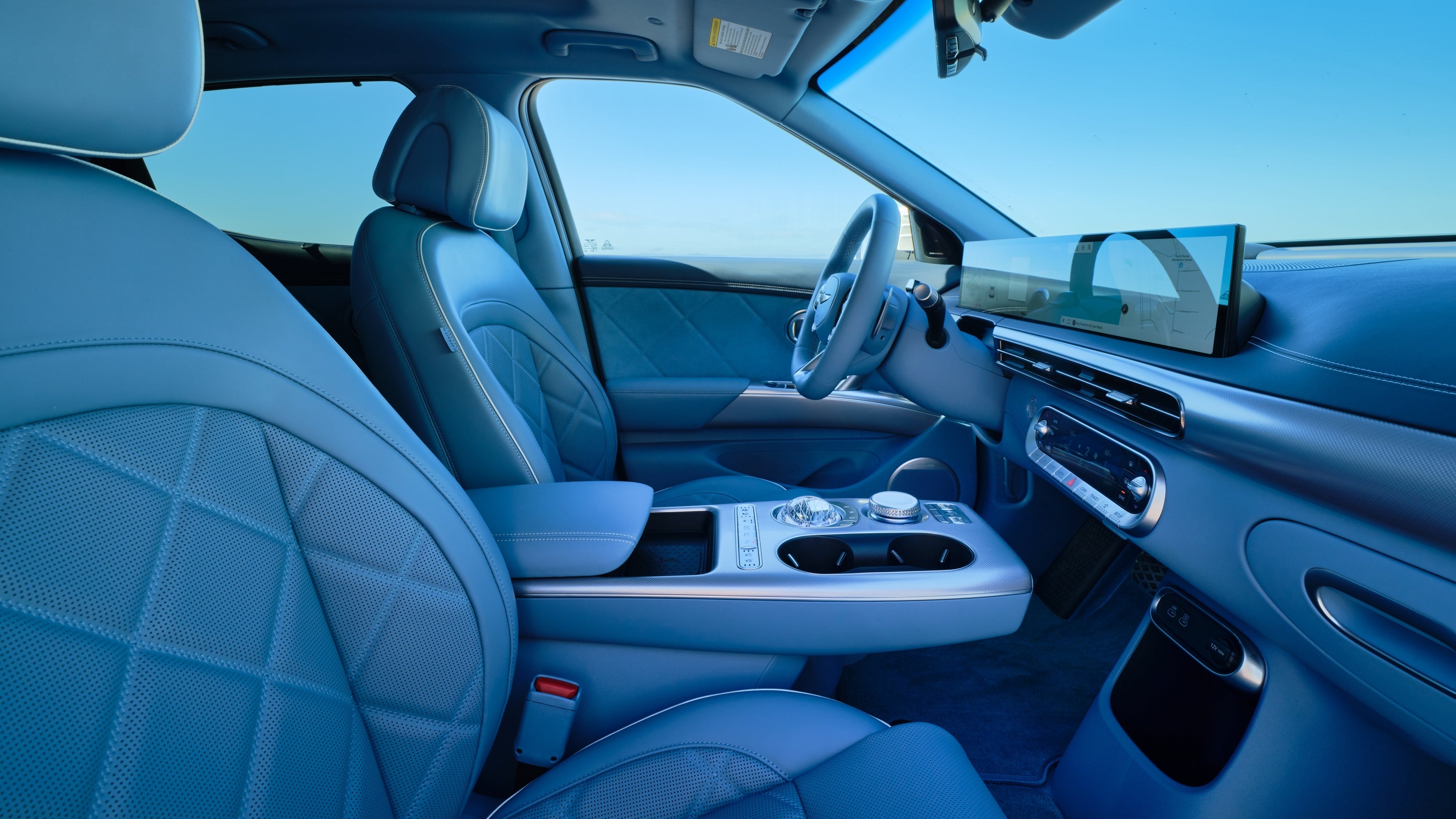 The beautiful aqua green interior of the new GV60 is shown from the passenger seat looking sideways at the drivers seat, front dash and console.
