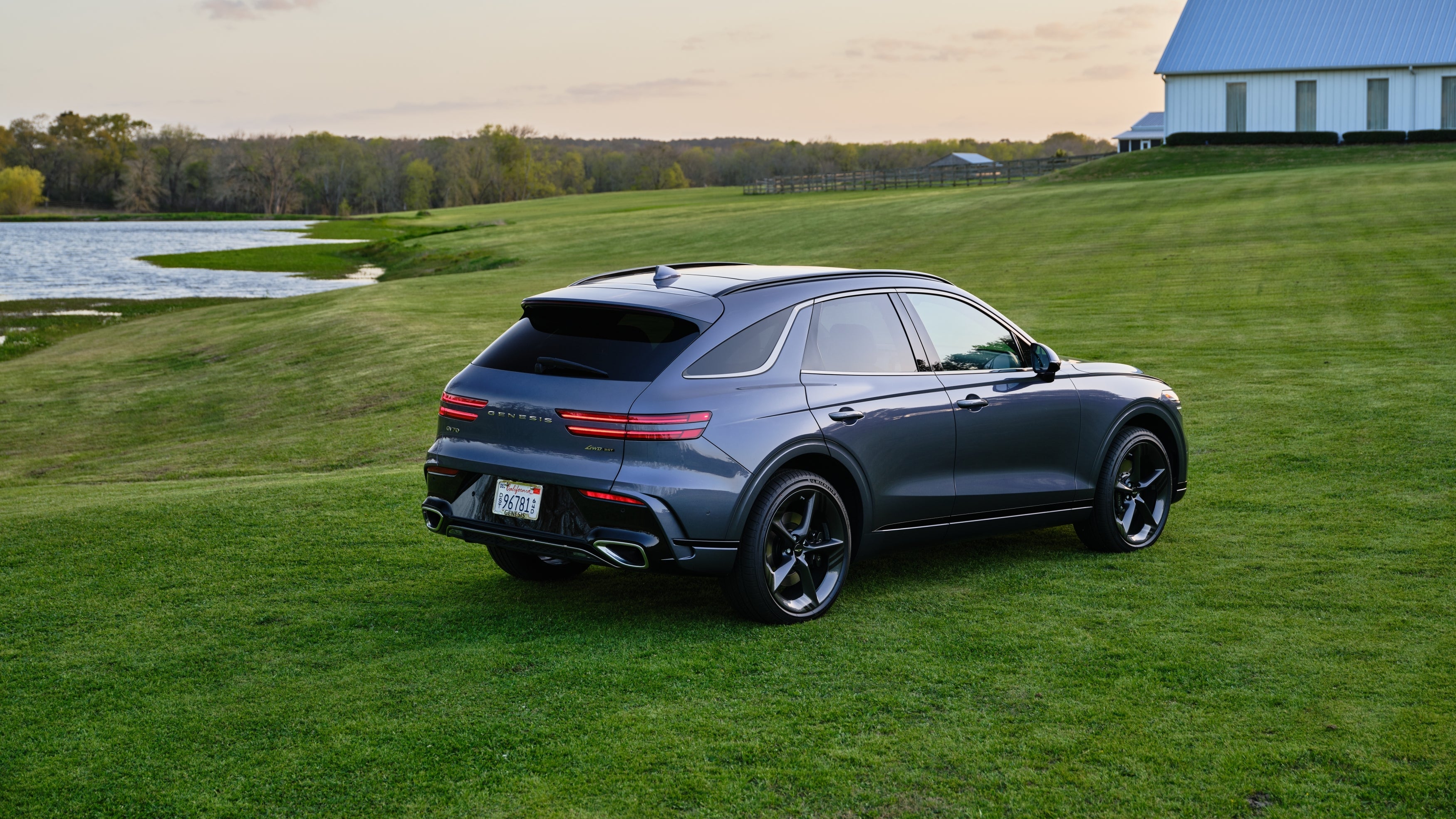 The new GV70 is parked turned away from the viewer to the right on a large grass field by the edge of a pond.