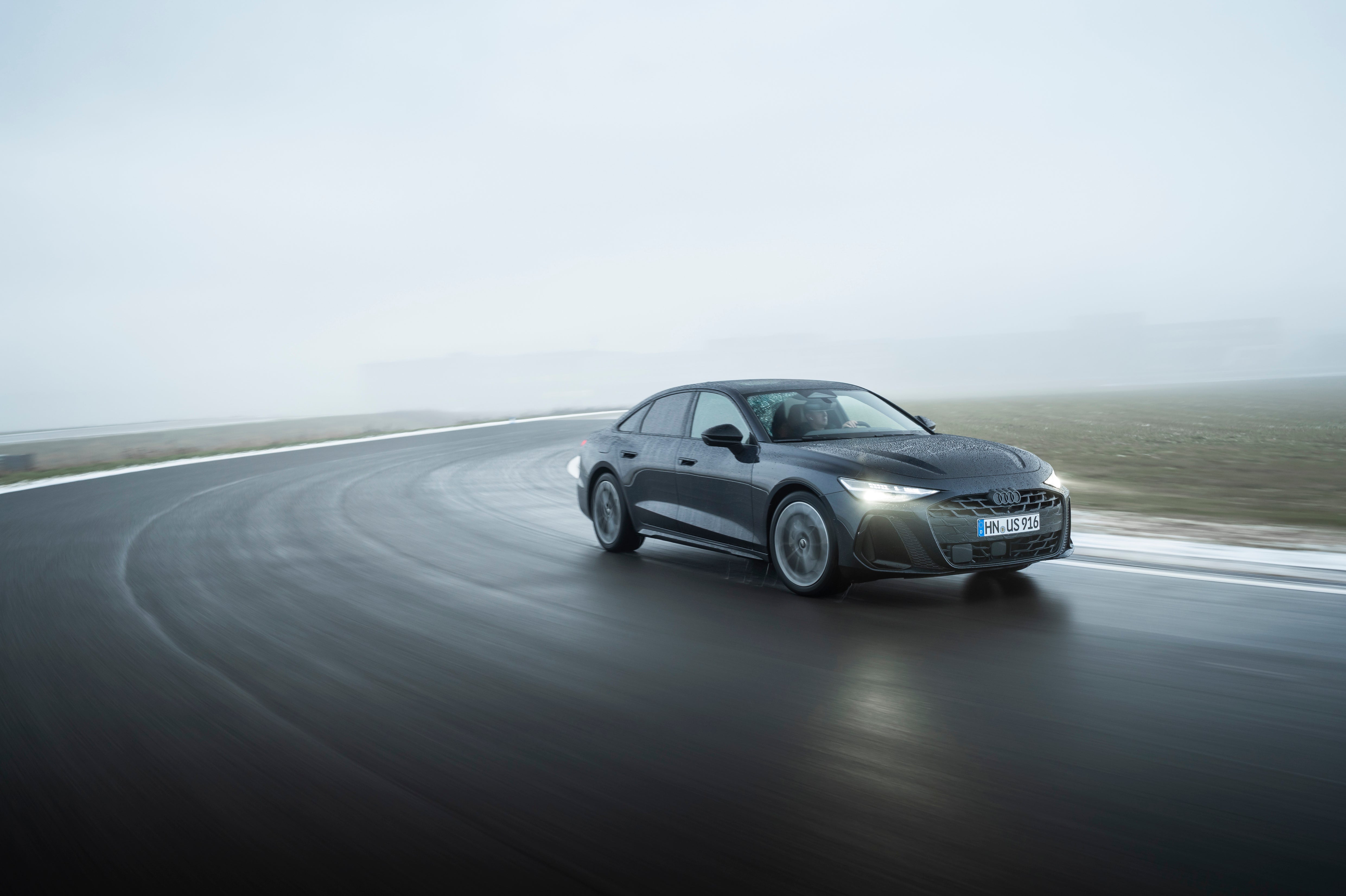 A grey 2026 Audi A6 in Scottsdale drives towards the viewer to the right on a racetrack in the rain.