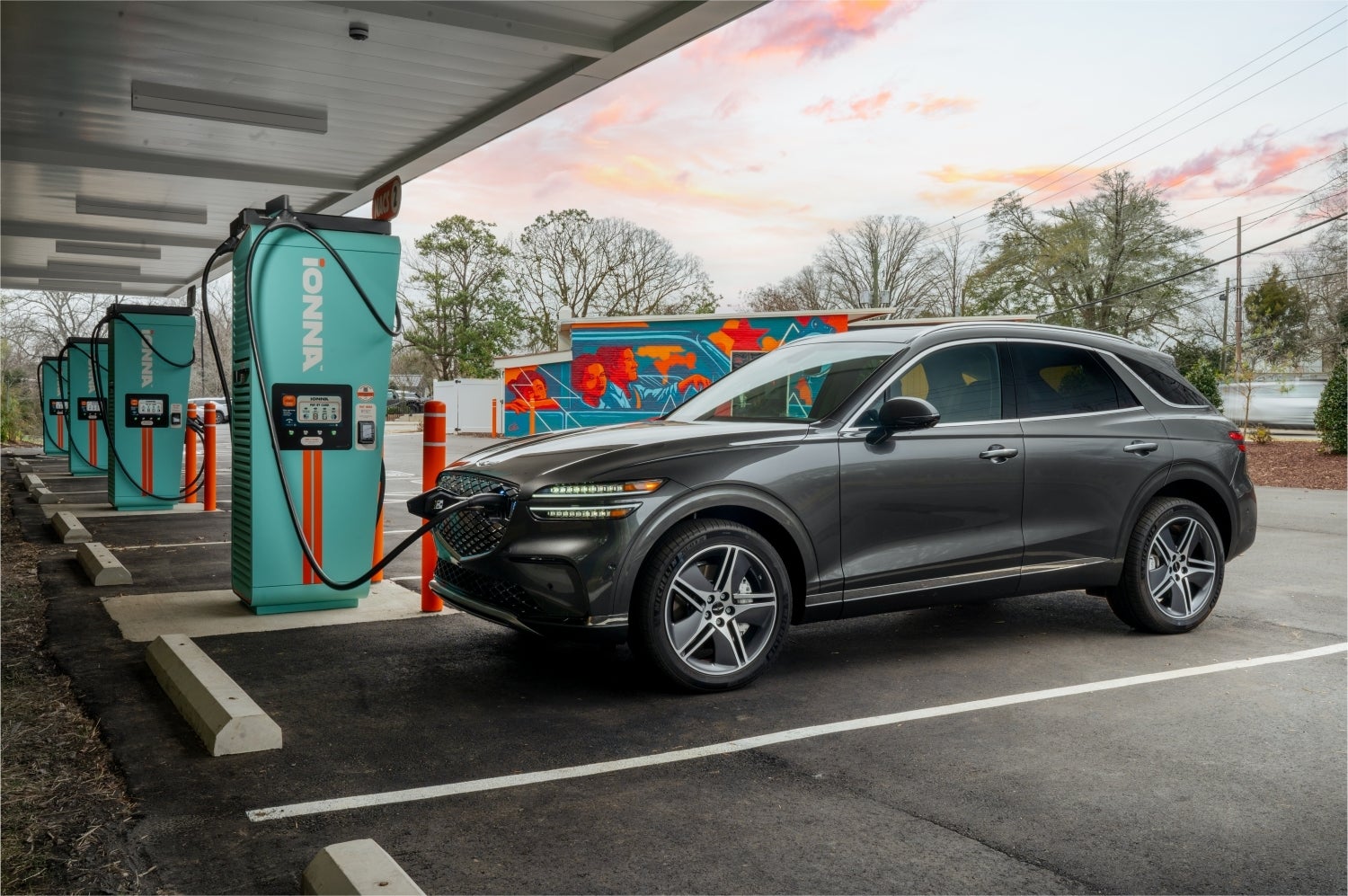 A savile silver is parked at a former gas station using an electric charger, showing the driver's side of the Genesis EV in Phoenix.