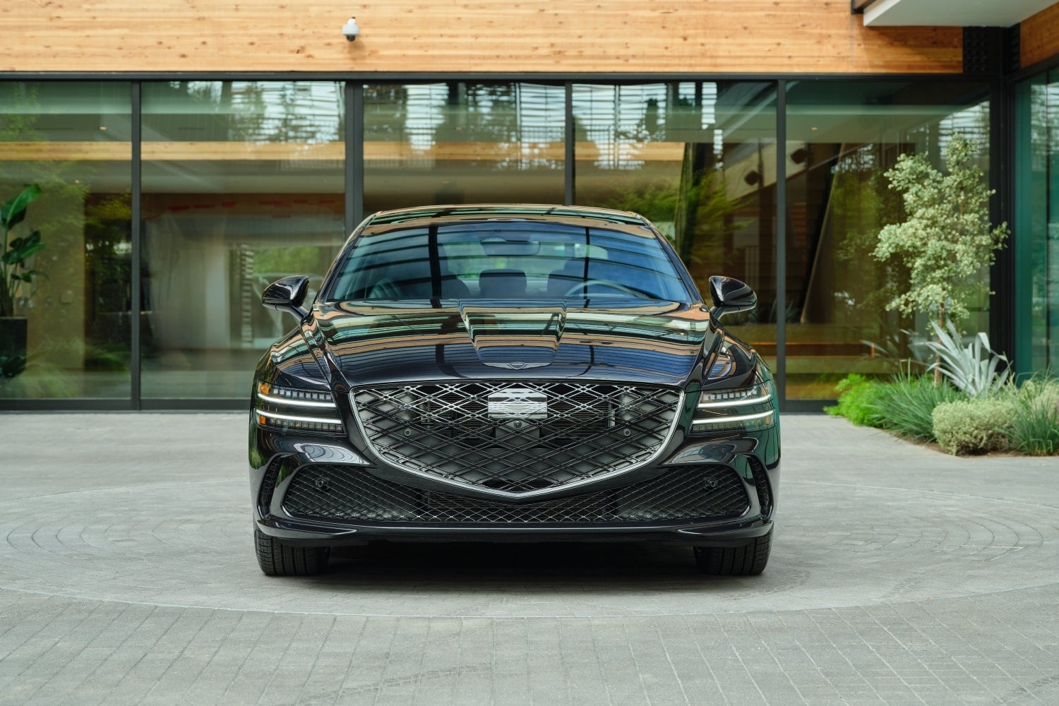 A black 2026 Genesis G80 in Scottsdale is parked facing the viewer on a tiled driveway in front of a modern building.