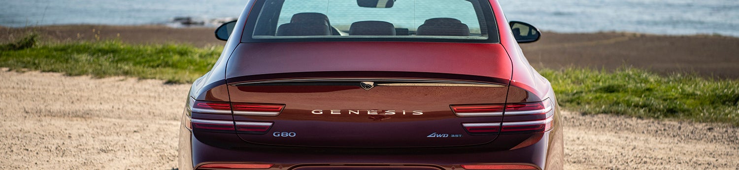 Rear view of a red Genesis G80 parked near the ocean.
