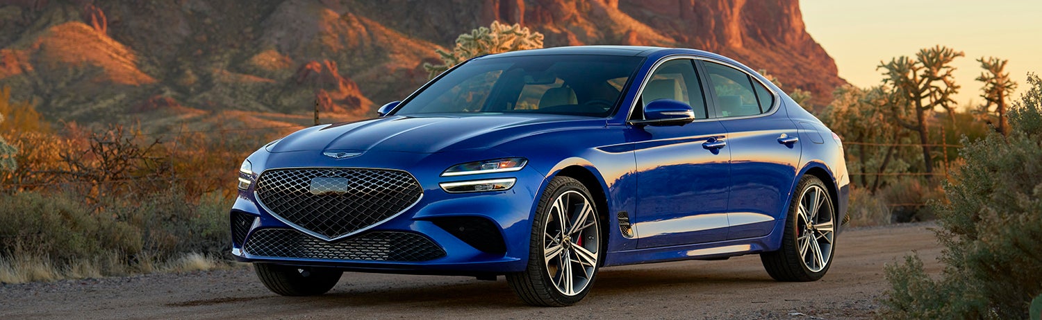 A blue Genesis G70 parked on a desert road.